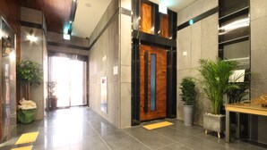 Un vestíbulo moderno con puerta de madera, plantas en macetas y mostrador de recepción.