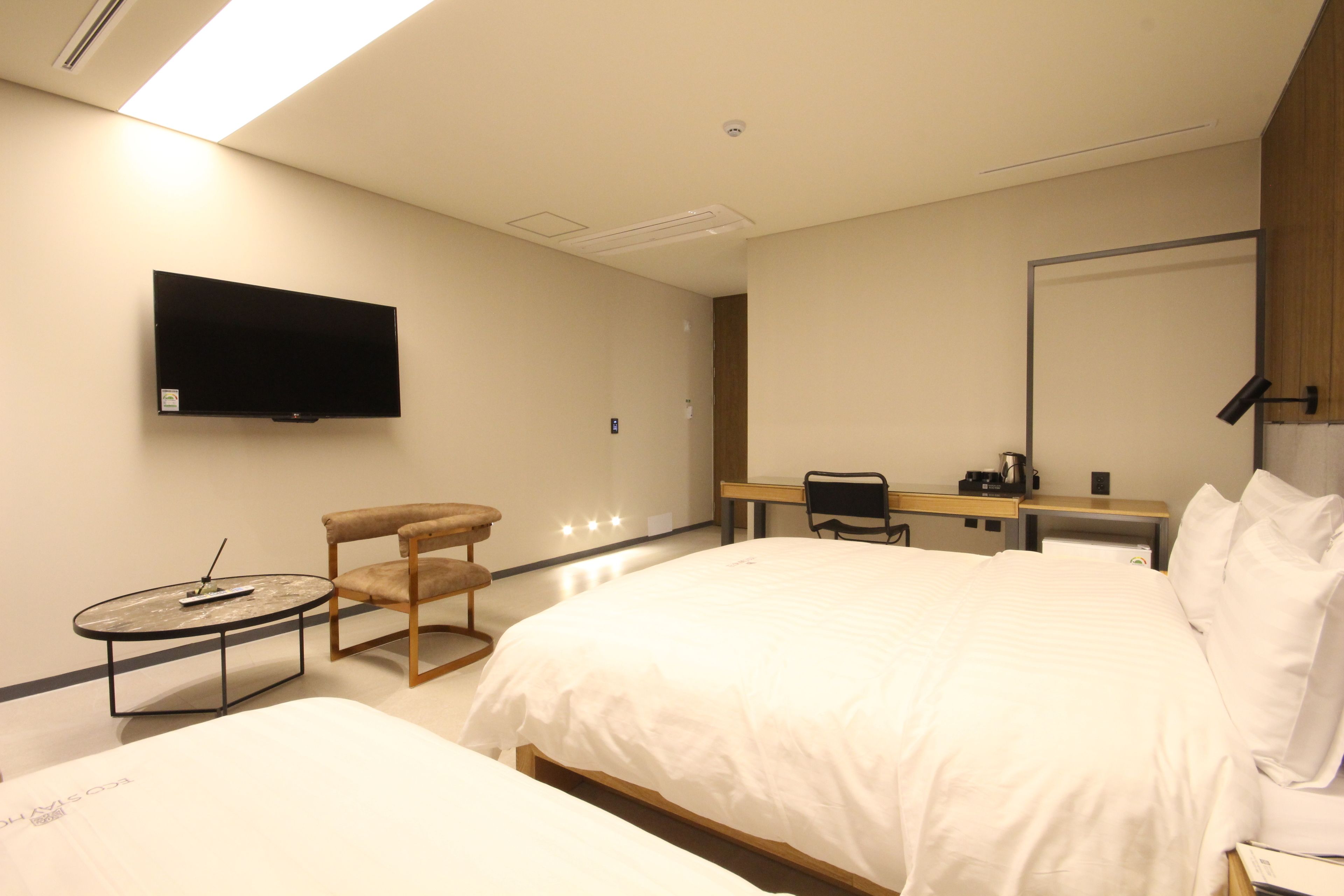 Een hotelkamer met een groot bed, een bureau met stoel, een aan de muur bevestigde televisie en een kleine tafel met stoel.