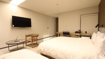 Een hotelkamer met een groot bed, een bureau met stoel, een aan de muur bevestigde televisie en een kleine tafel met stoel.