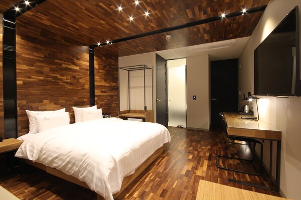 A modern hotel room with a wooden ceiling, a large bed with white linens, a desk with a chair, and a large mirror. - Ecostay Hotel (Jeonju)