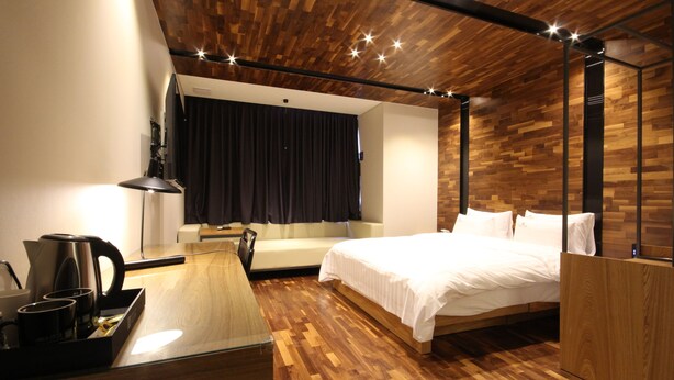 Una habitación de hotel moderna con techo de madera, cama, sofá, escritorio con cafetera y espejo.