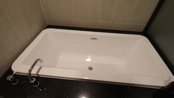 Une baignoire rectangulaire, dotée d’un robinet et d’un drain, placée contre un mur carrelé.
