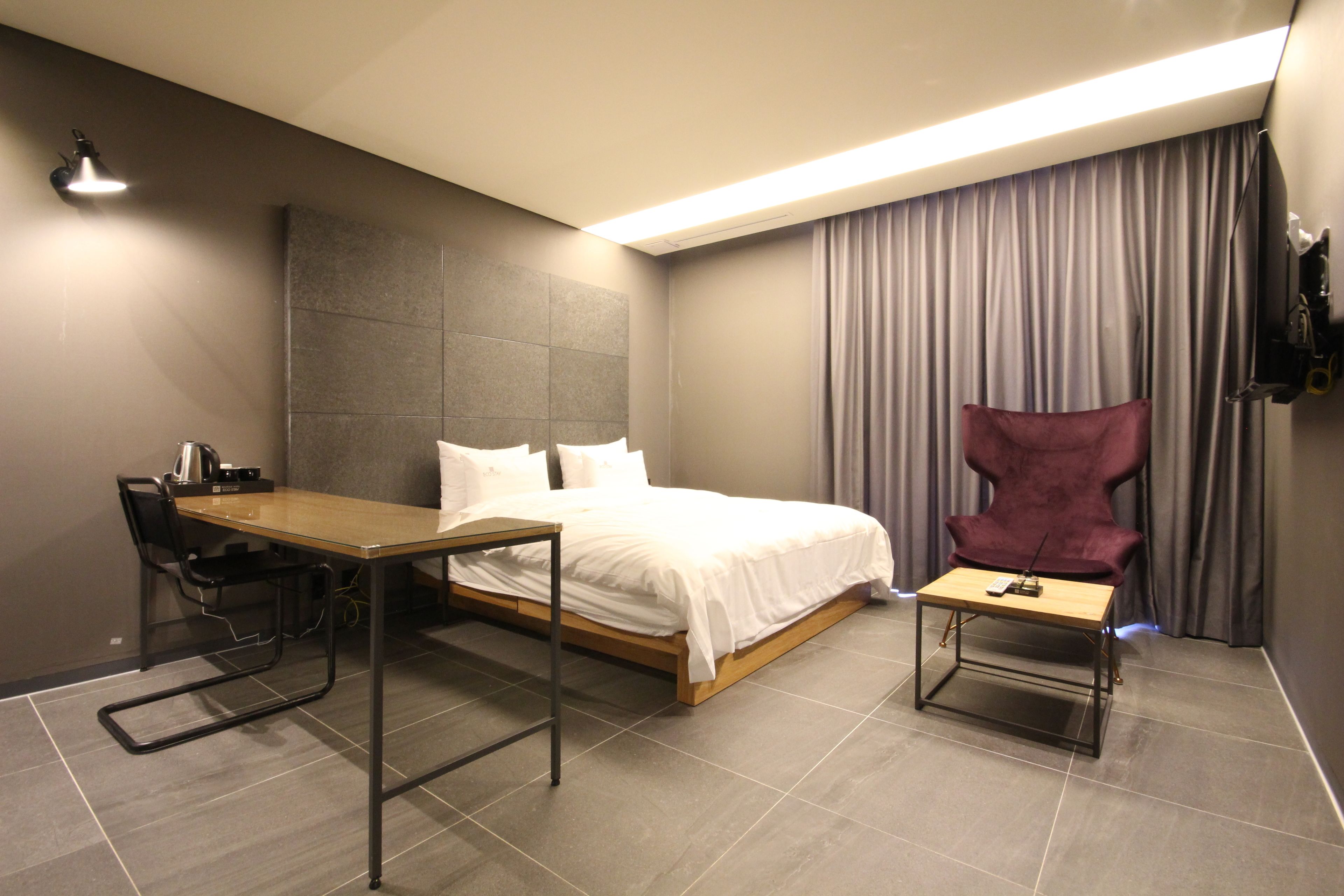 A modern hotel room with a bed, a desk, a chair, and a TV.