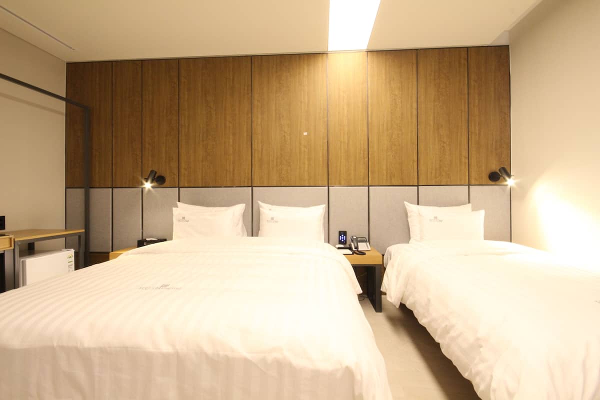 A hotel room with two beds, a wooden headboard, bedside lamps, and a small desk with a telephone.