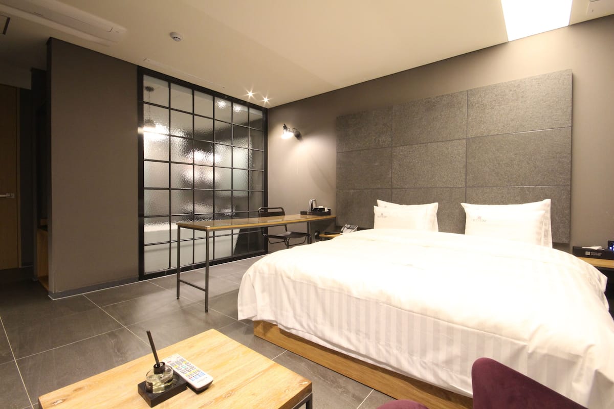 A modern hotel room with a large bed, a desk, and a seating area with a view through a glass partition.
