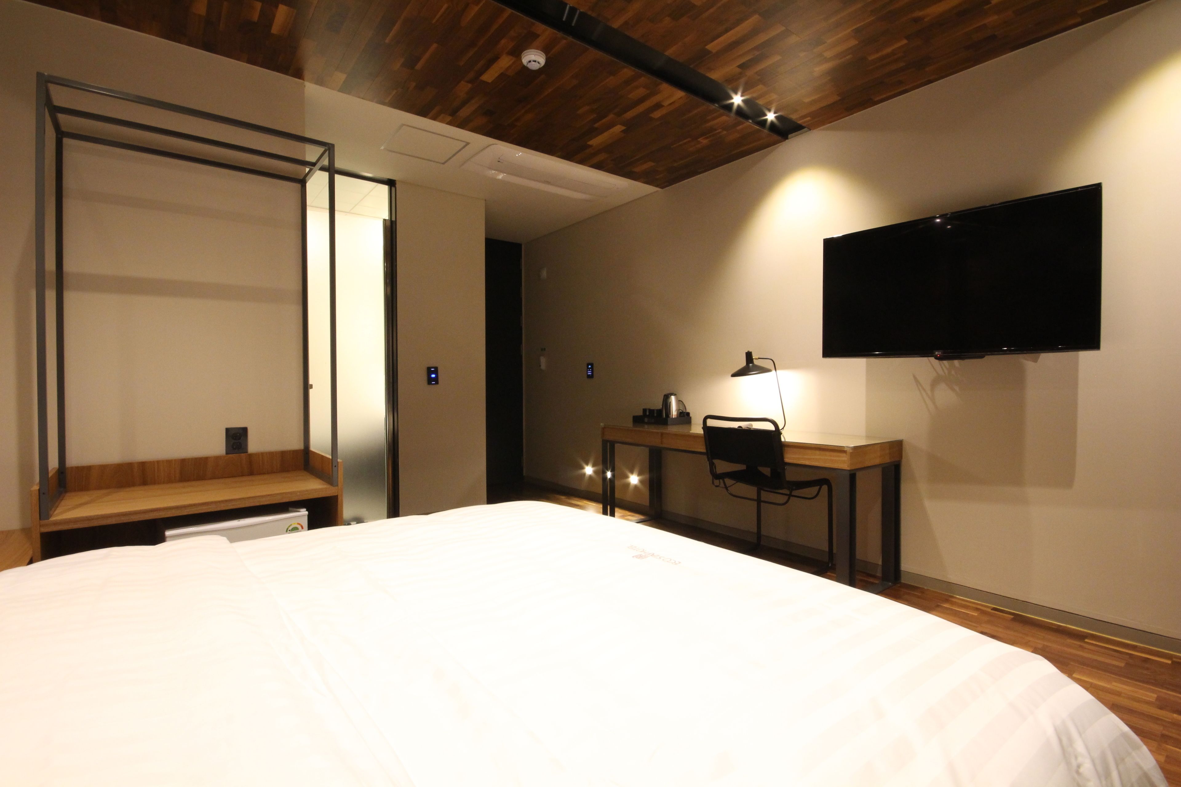 Habitación de hotel con cama, escritorio con silla, televisor de pantalla plana en la pared y techo de madera.