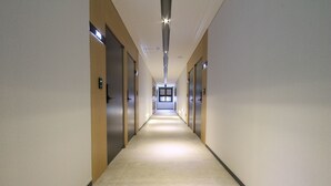 Un largo y estrecho pasillo con puertas a ambos lados, que conduce a una habitación luminosa al final.