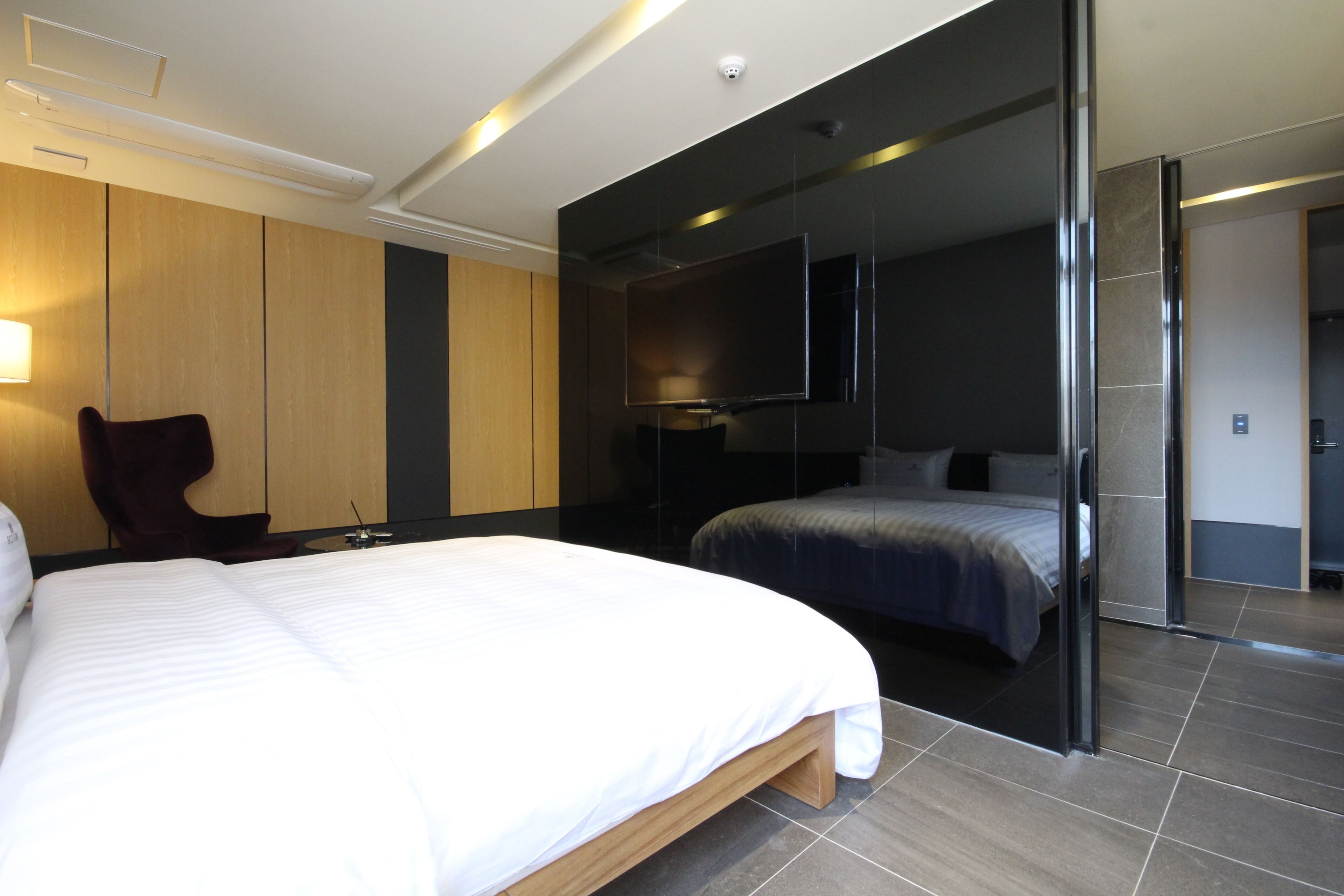 A modern hotel room with a large bed, a chair, a flat-screen TV, and a separate sleeping area.
