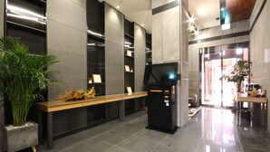 Un área de recepción con un banco de madera, un quiosco digital y una planta en maceta.