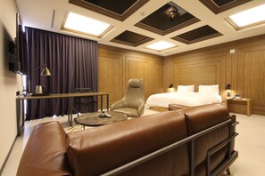 Una habitación de hotel moderna con una cama grande, un sofá de cuero, un escritorio con lámpara y un televisor en la pared.