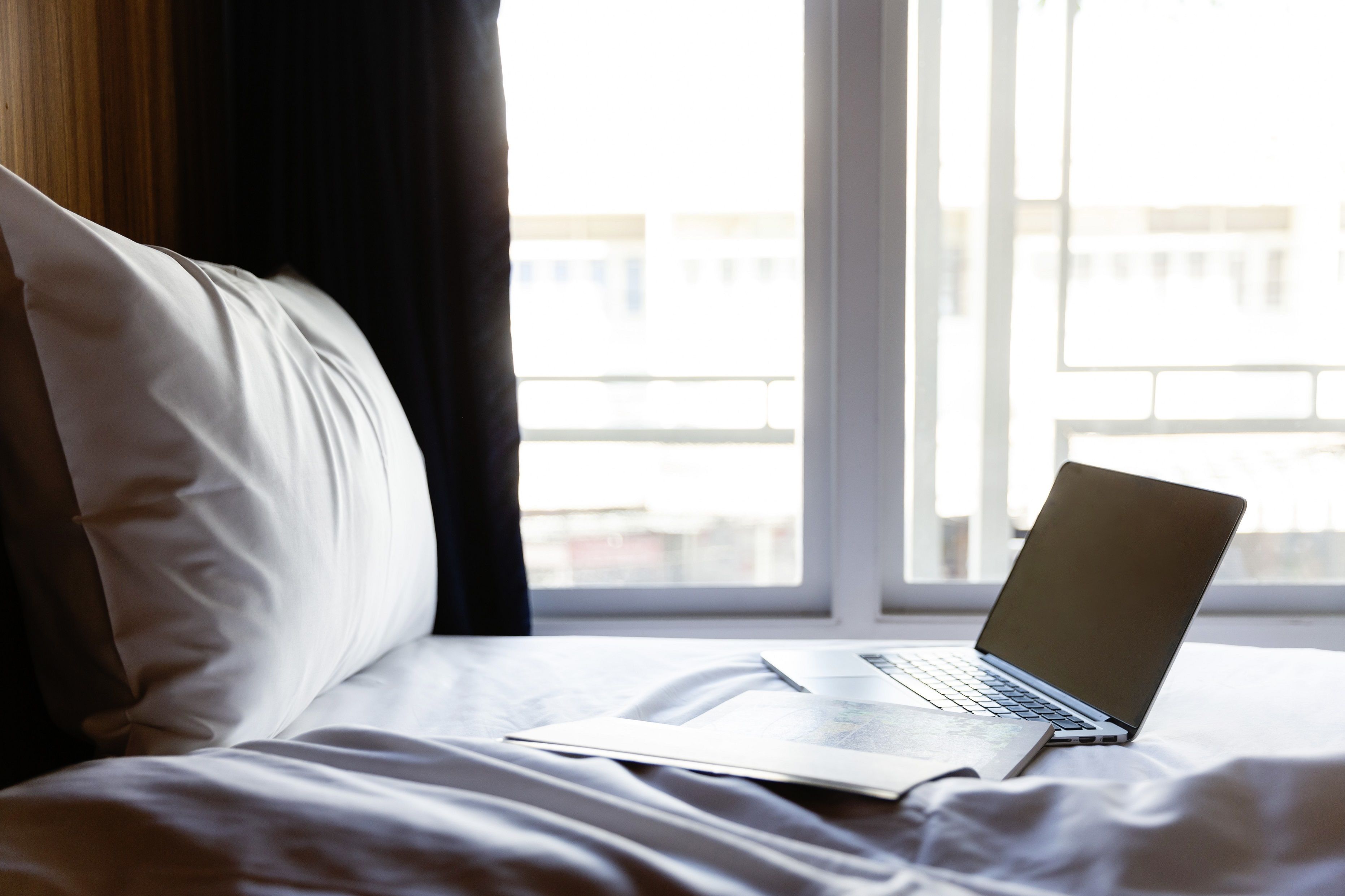 A laptop on a bed with a window in the background.