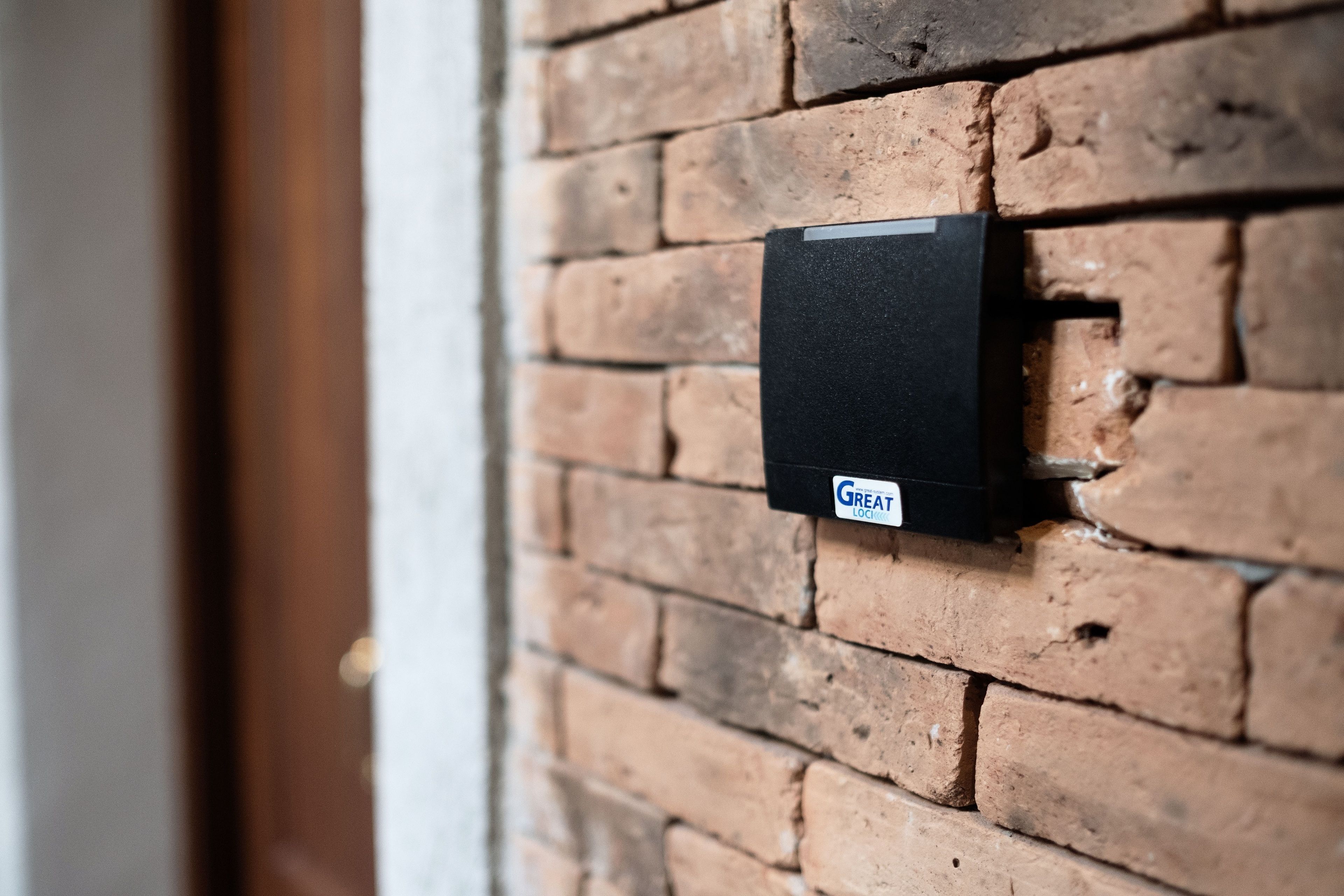 Un portero automático negro instalado en una pared de ladrillo.