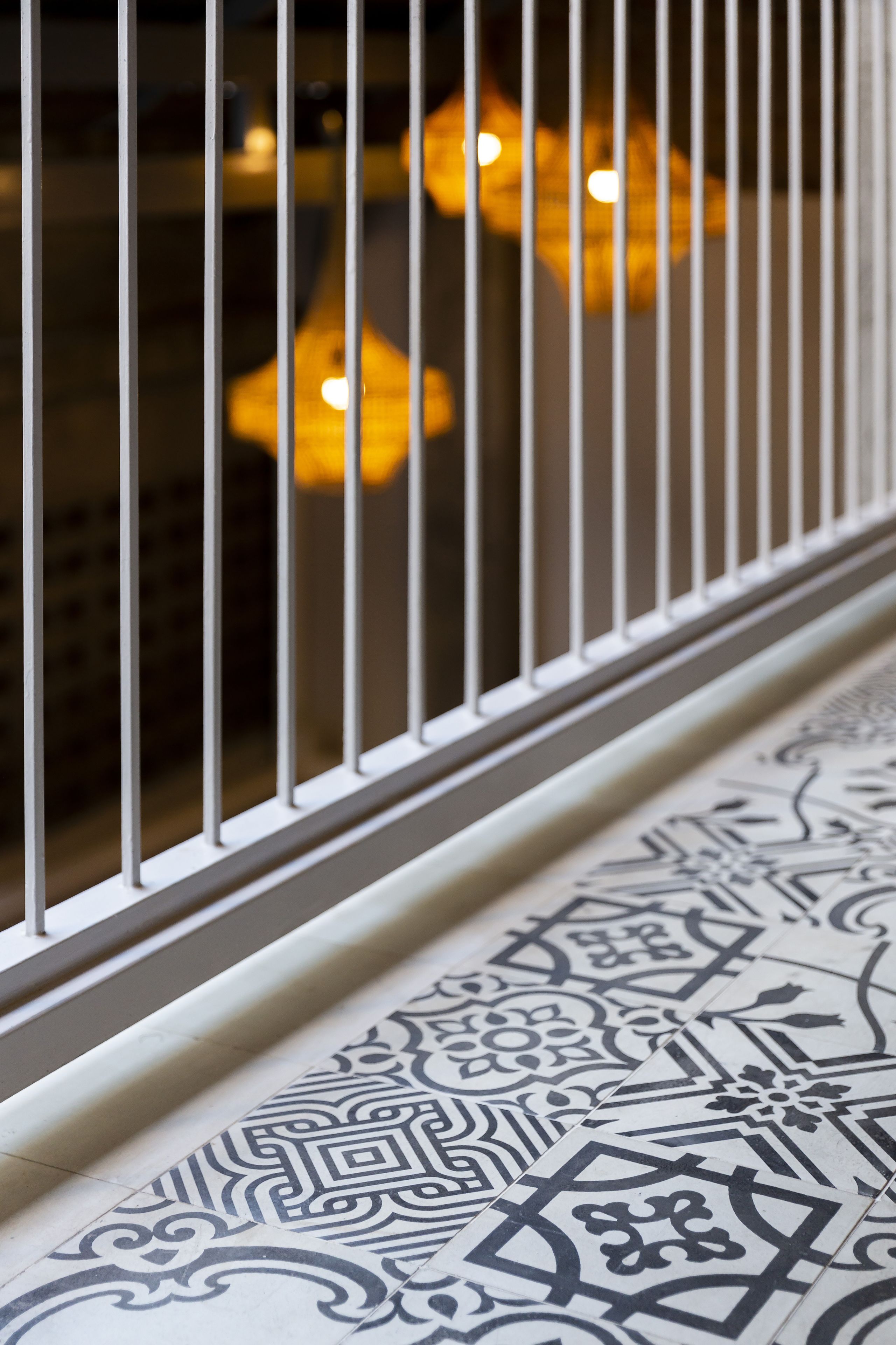 A close-up of a white metal railing with a patterned floor below.