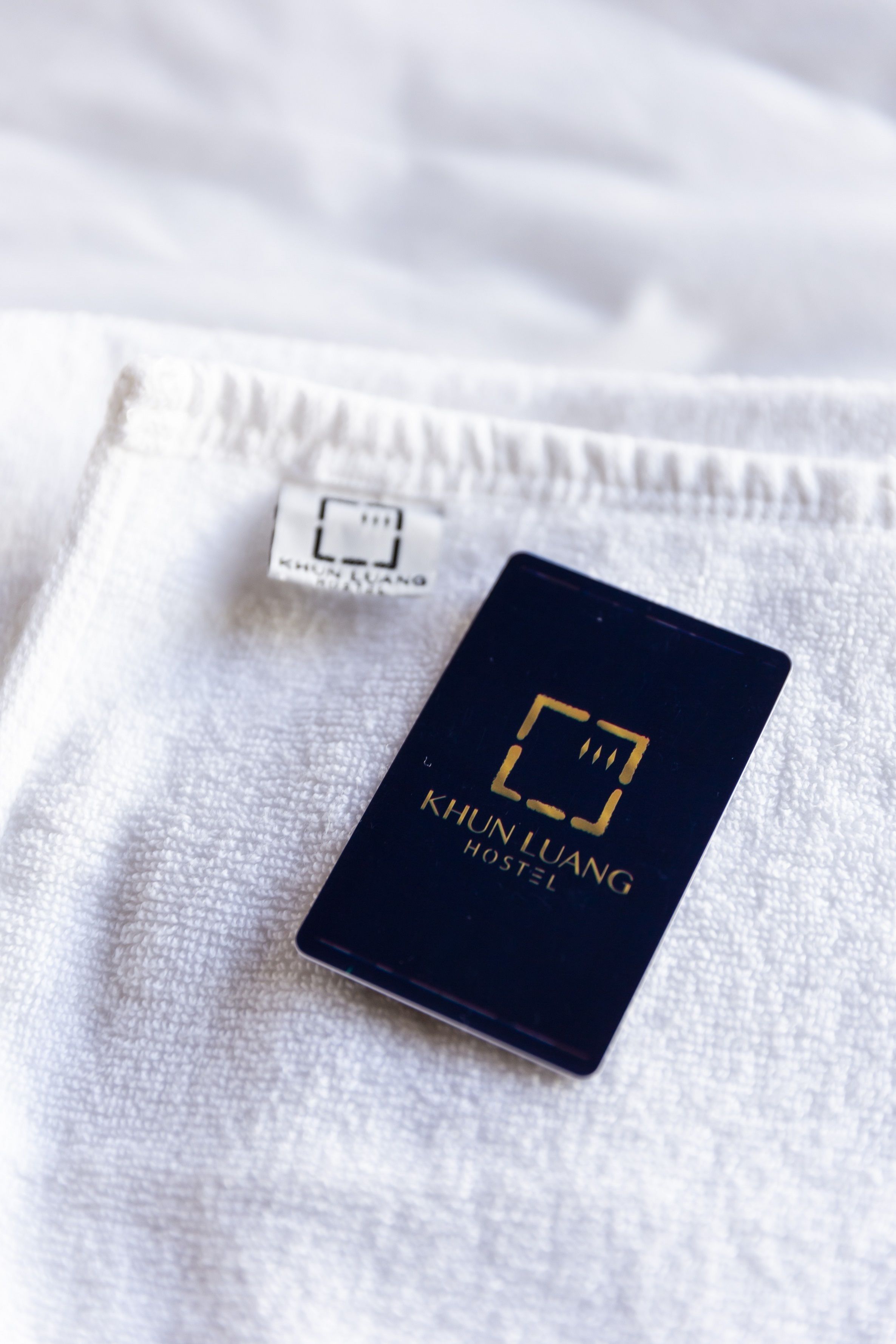A black card with the text "KHUN LUANG HOSTEL" on a white textured surface.