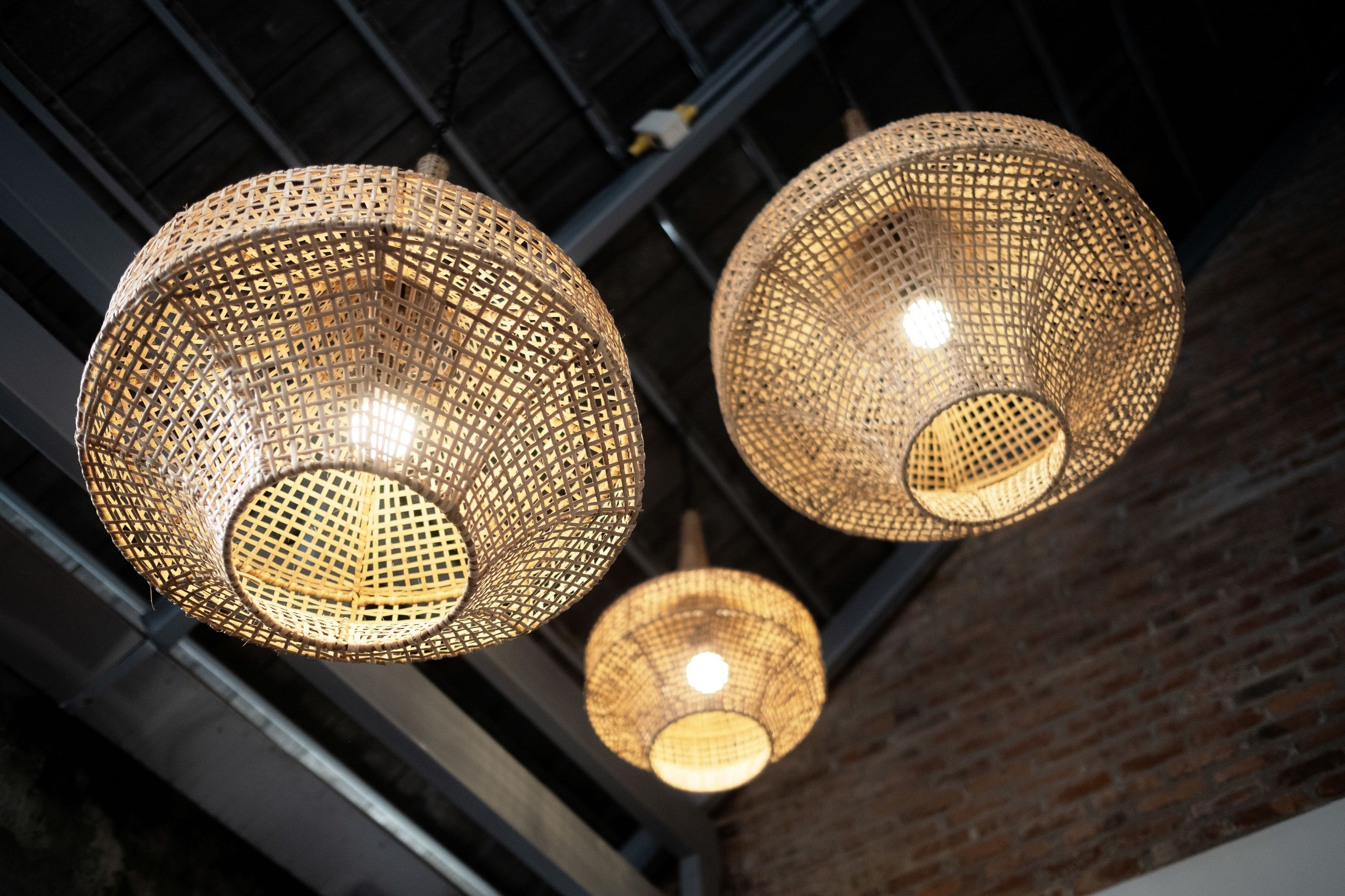 Three spherical wicker pendant lights hanging from a ceiling with a brick wall in the background.
