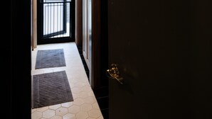 Un couloir avec une porte sombre, une porte vitrée au fond, et des lampes suspendues.