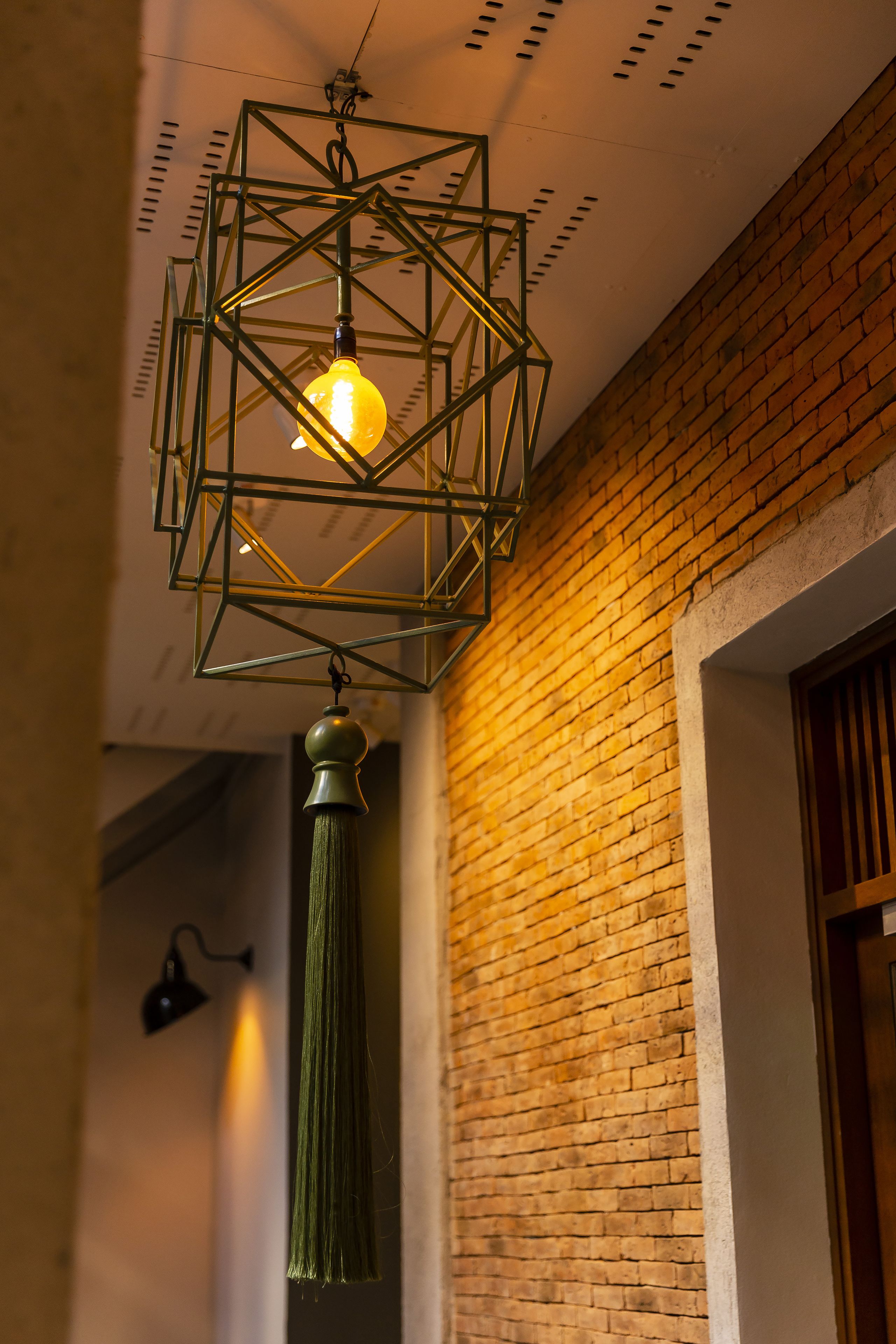 Een geometrische metalen lamp met zichtbare gloeilamp en een belsnoer eronder.