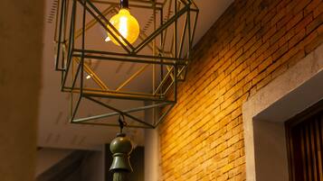 Un luminaire en métal aux formes géométriques, doté d’une ampoule visible et d’une frange pendant en dessous.
