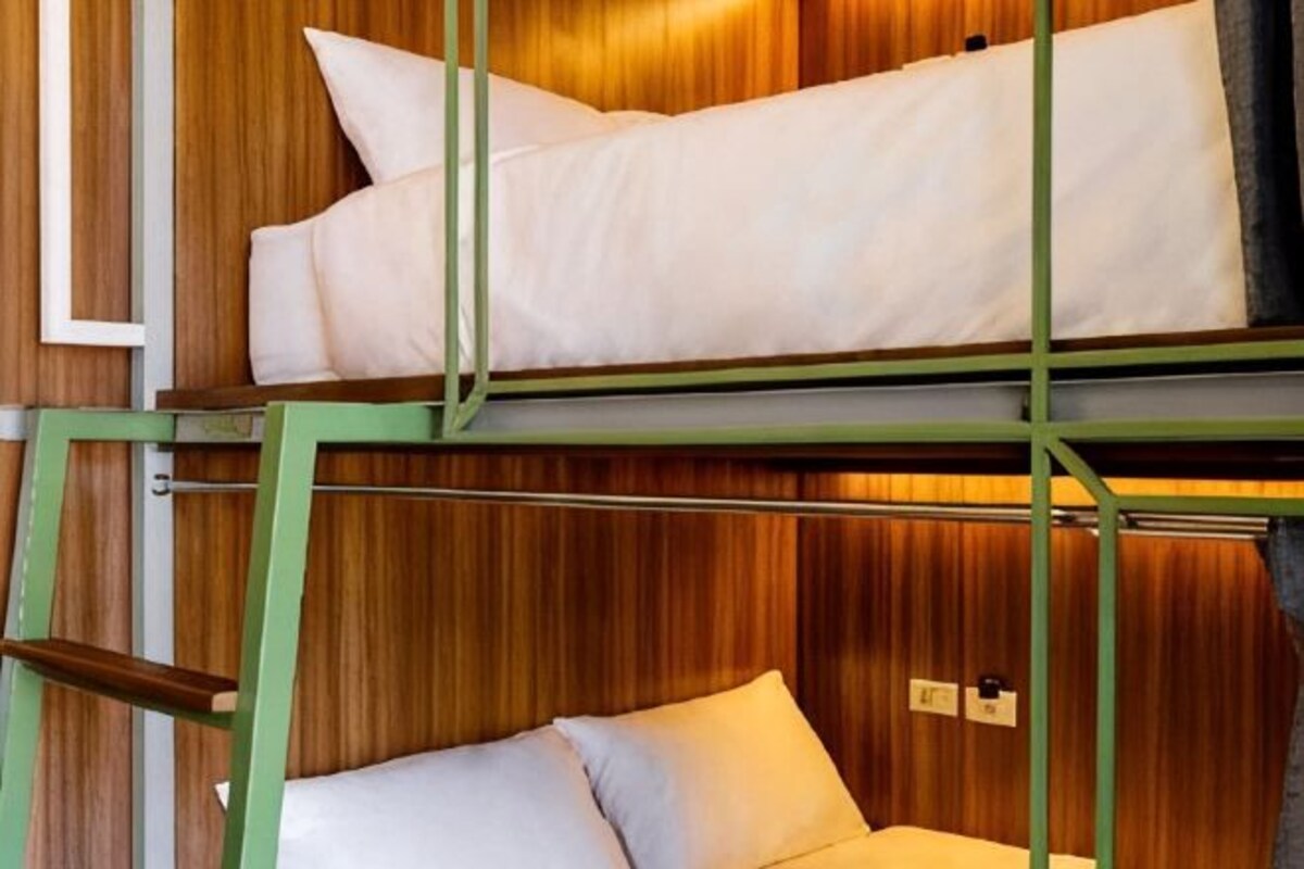 Un lit superposé avec deux oreillers, un revêtement mural en bois et une structure métallique verte.