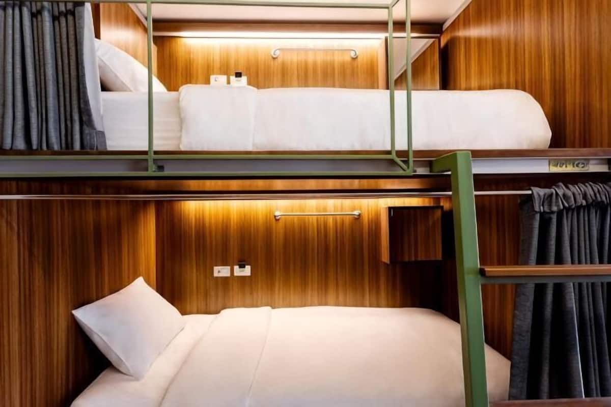 Quarto com beliche, painéis de madeira, escrivaninha rebatível e um pequeno armário.