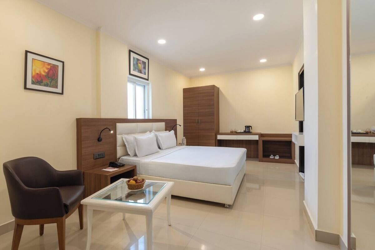 A modern hotel room with a large bed, a desk, a chair, and a small table with a fruit bowl.