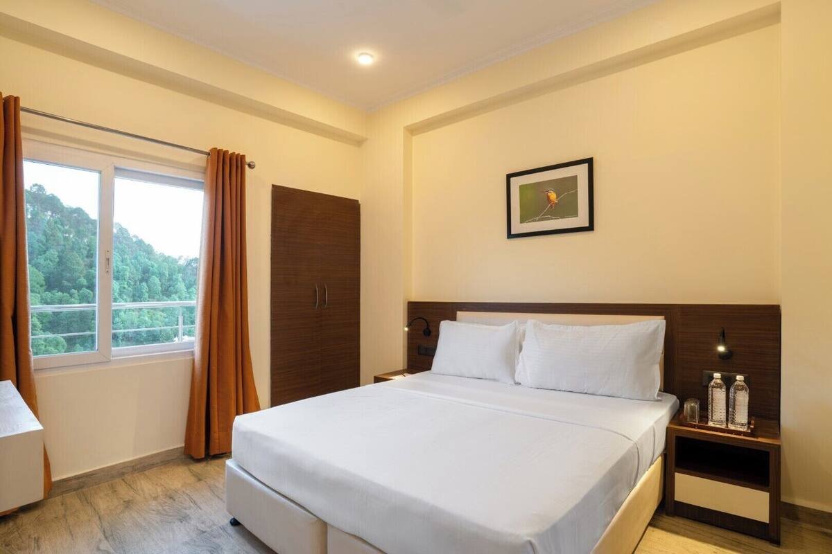 A hotel room with a bed, a nightstand, a wardrobe, a window with curtains, and a framed picture on the wall.