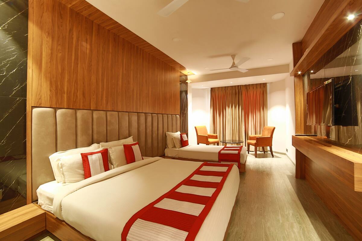 A hotel room with two beds, a seating area with chairs, a wooden desk, and a ceiling fan.