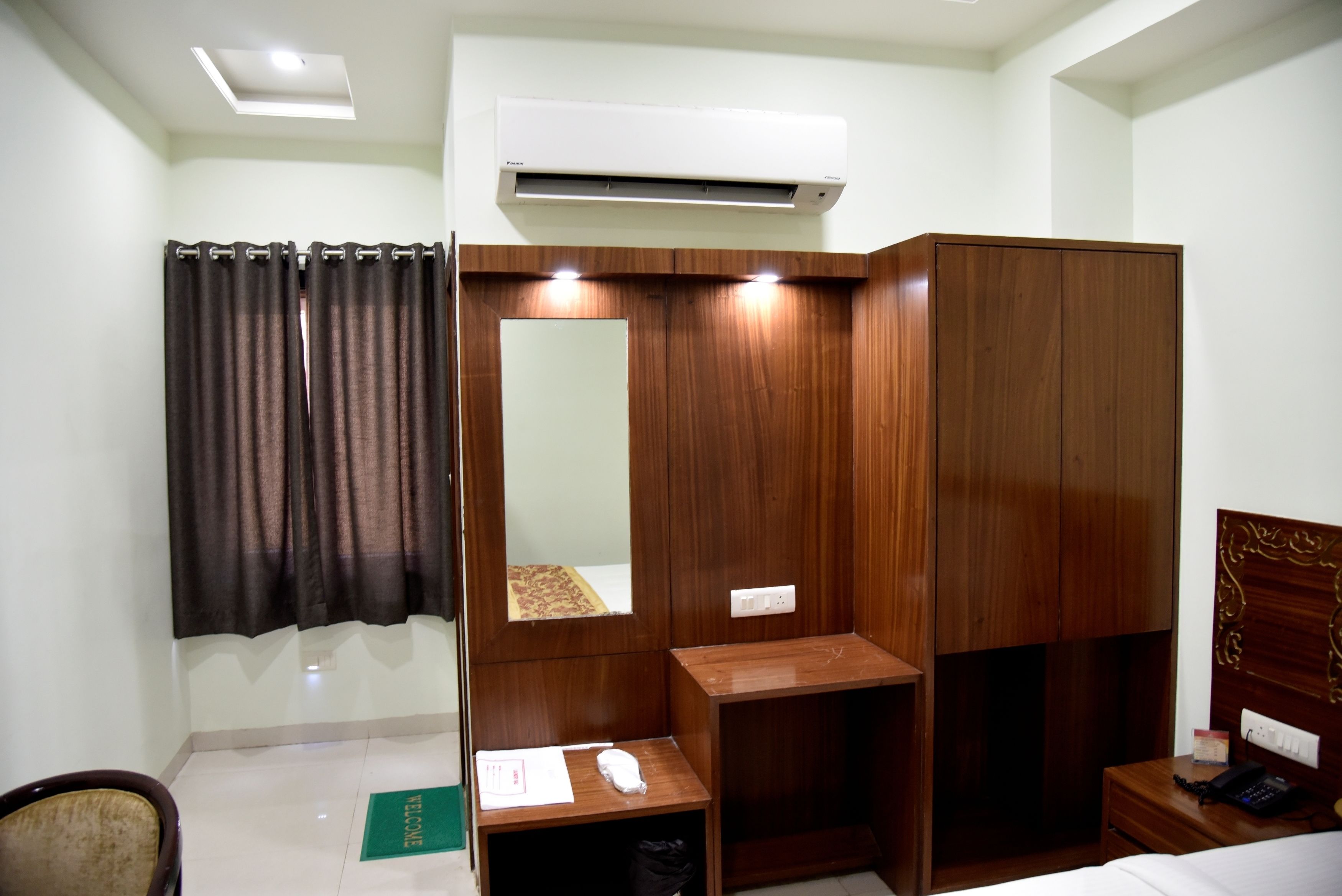 A hotel room with a wooden wardrobe, a bedside table, a mirror, and a bed.