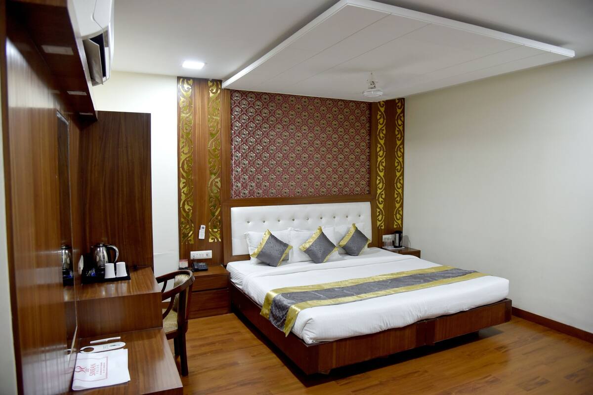 A hotel room with a large bed, wooden furniture, a desk, and a wardrobe.