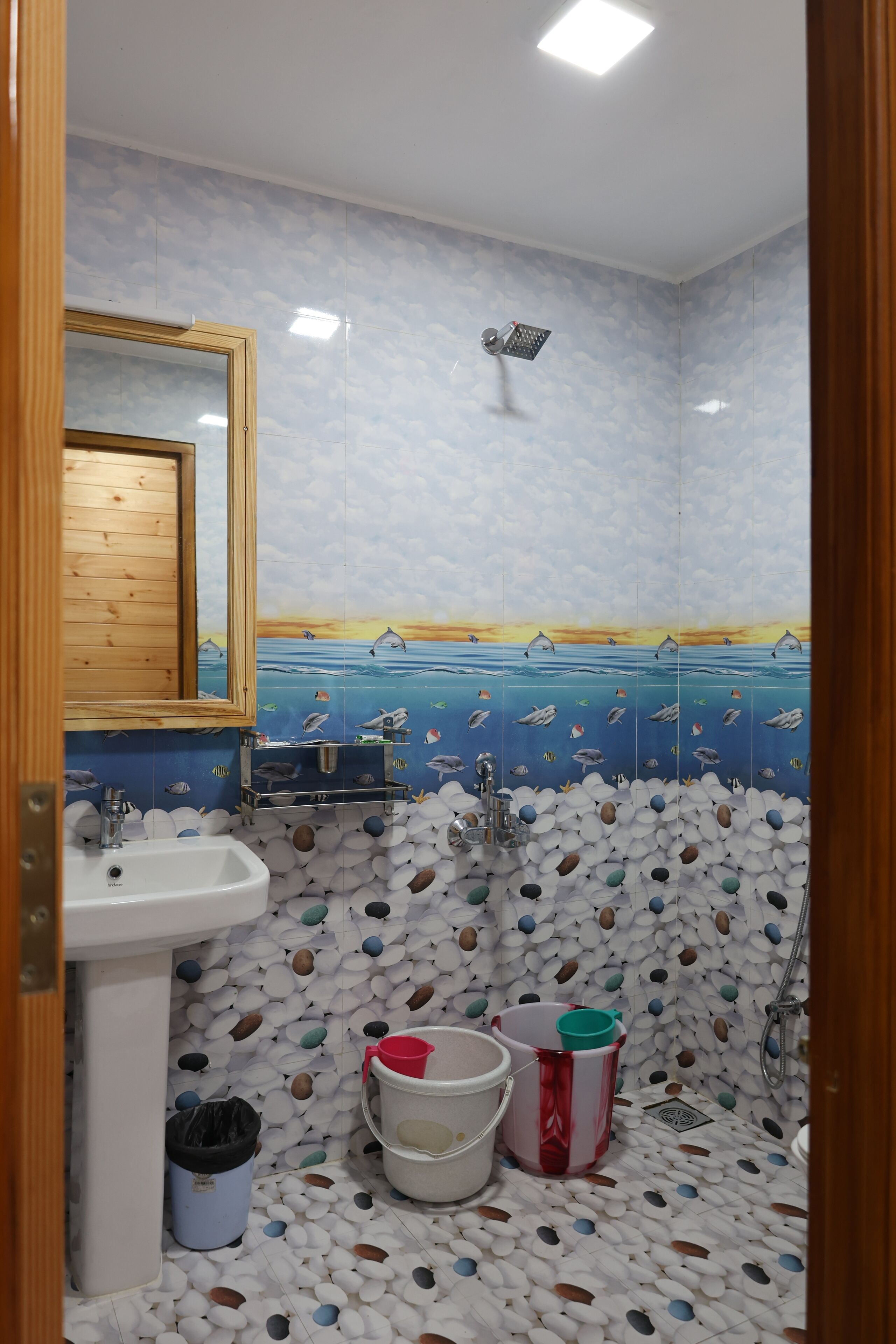 Un baño con suelo de baldosas que presenta un diseño de mar y cielo, un lavamanos, un espejo y una ducha.