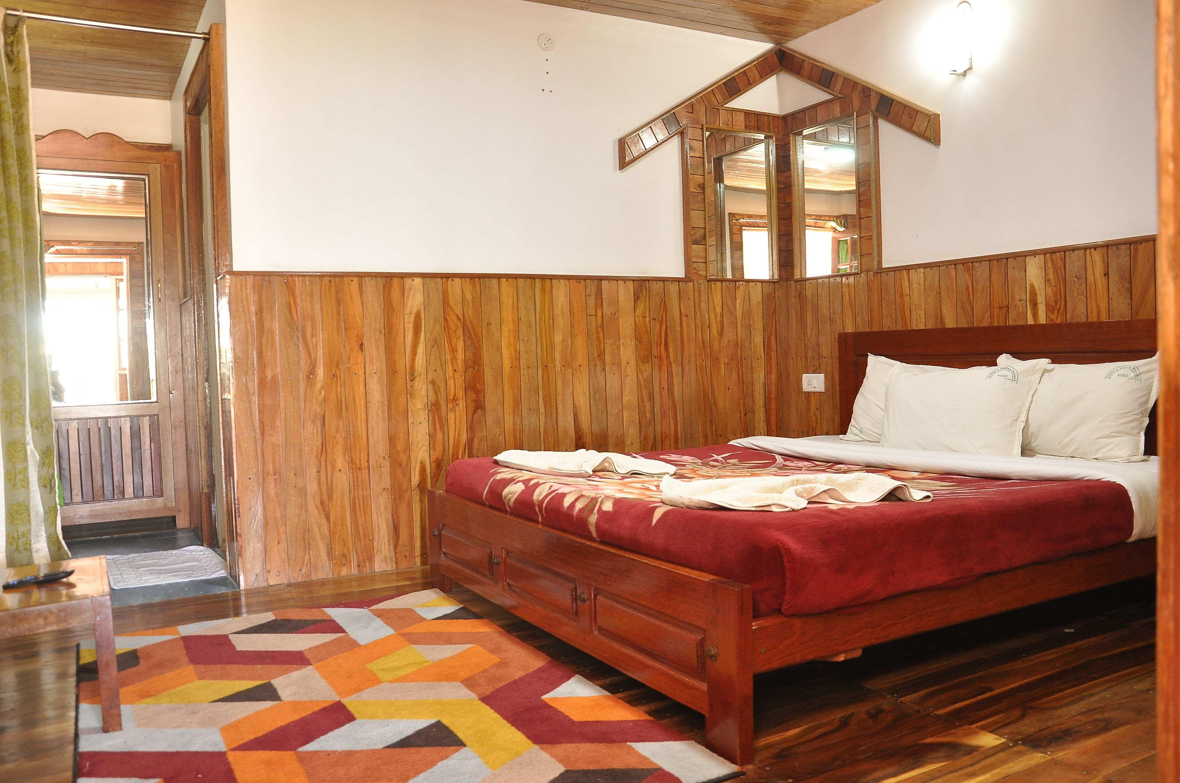 A wooden-paneled bedroom with a bed, a mirror, and a colorful rug.