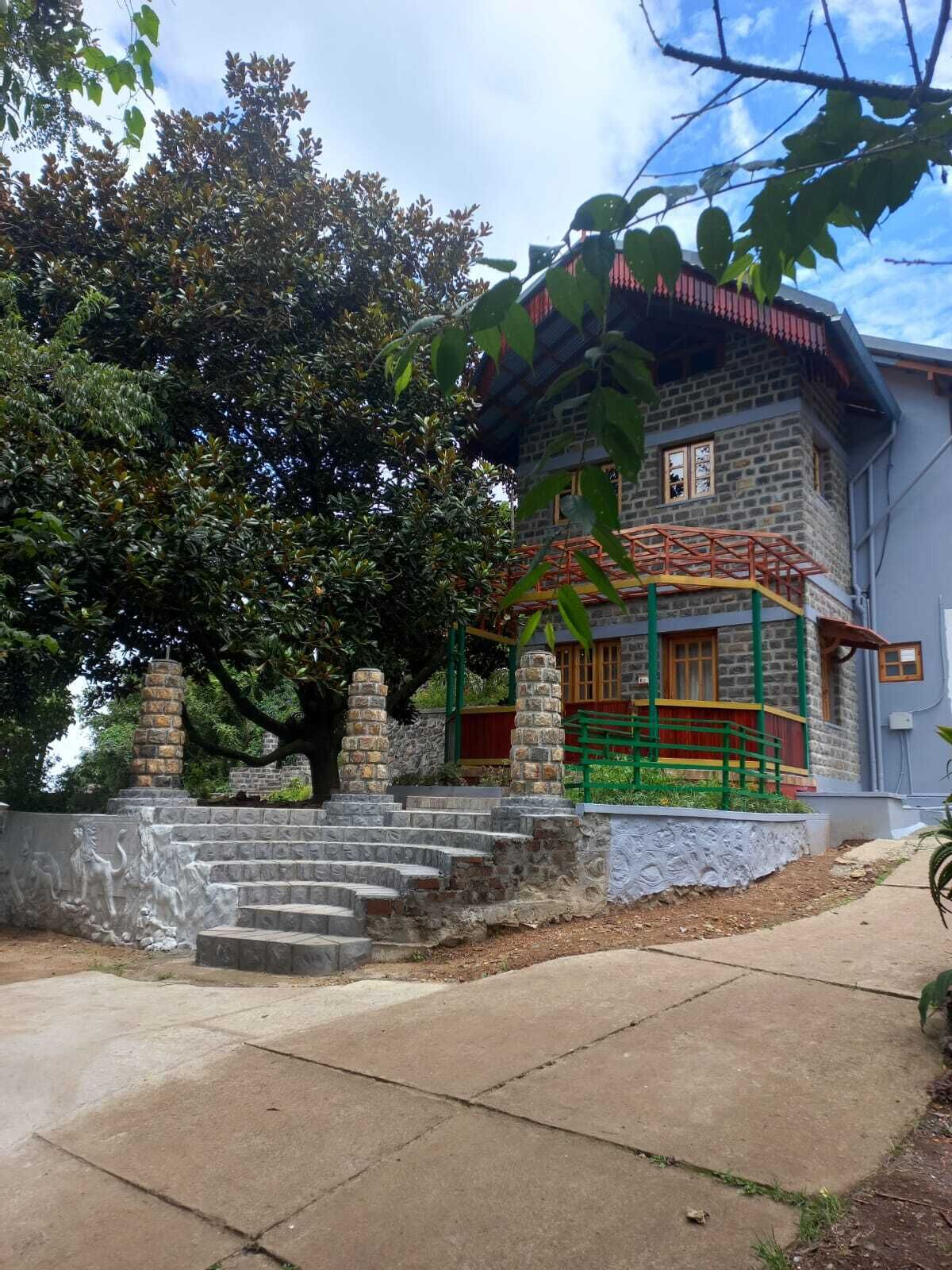 Un bâtiment en pierre avec un toit rouge, des balustrades vertes et un escalier menant à l’entrée.
