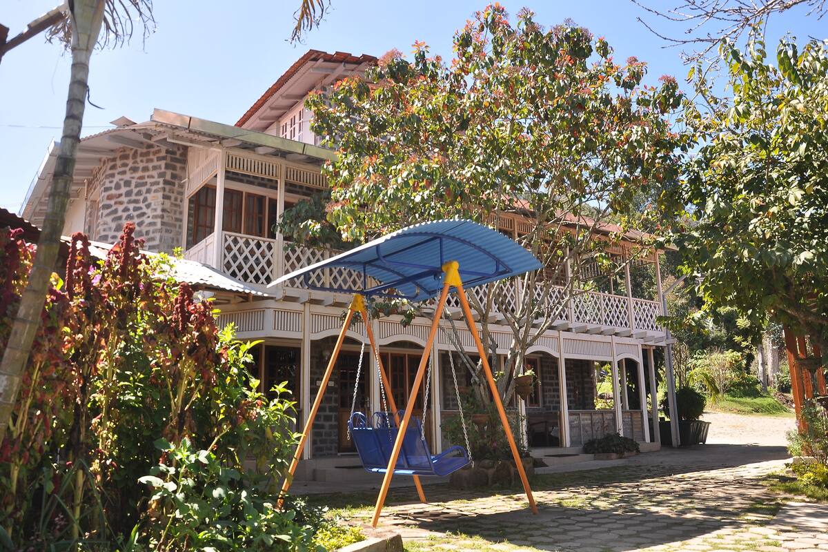 A stone house with a balcony, a swing set, and a covered seating area.