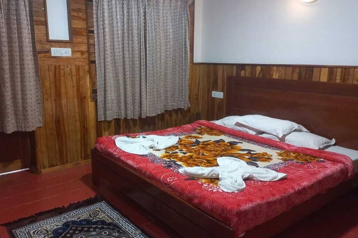 A bedroom with a wooden headboard, a red bedspread, and a patterned rug.
