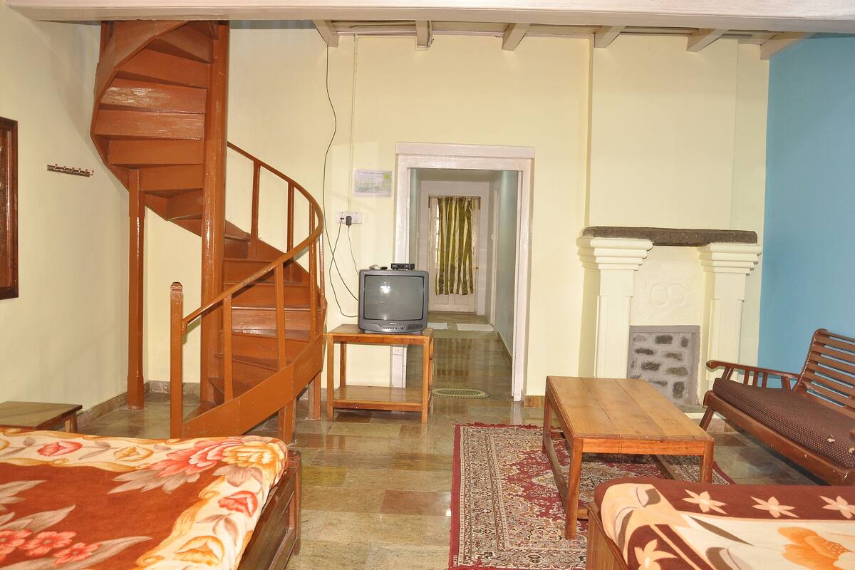 A room with a wooden staircase, a television on a small table, a fireplace, and a bed with a floral bedspread.