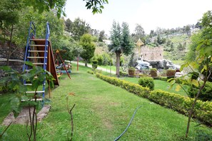 A well-maintained garden with a children's play area, neatly trimmed hedges, and a stone structure resembling a castle. - Lillysvalley Resort (Kodaikanal)