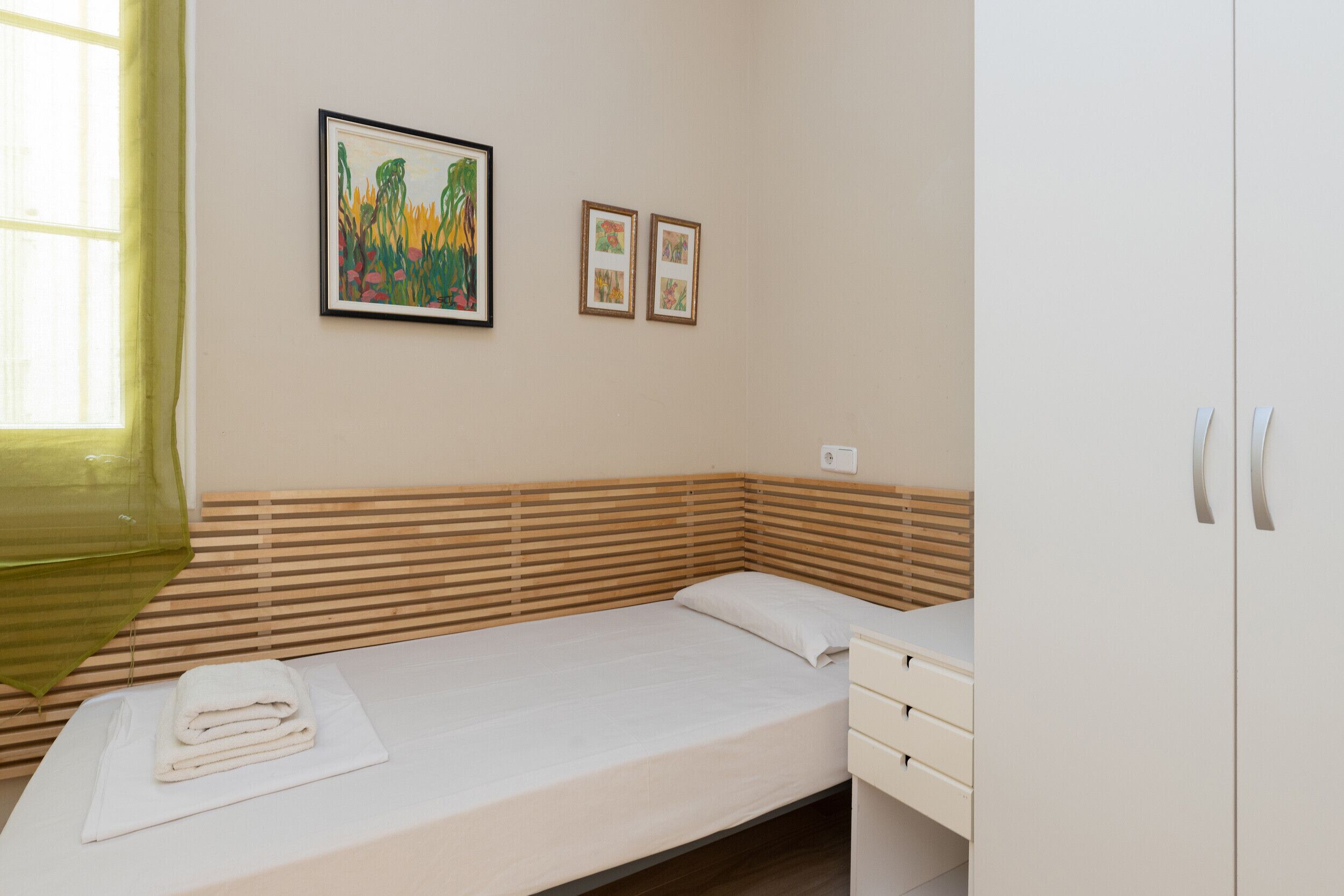 A neatly made bed with a folded towel, a bedside table with a drawer, and two framed pictures on the wall.