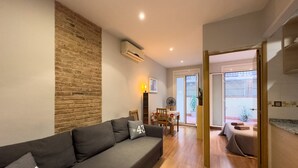 Uma sala de estar moderna com um sofá cinzento, uma parede de tijolos decorativa, um espaço de refeições com mesa e cadeiras, e uma porta de vidro deslizante que dá para uma área externa.