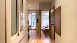 Um corredor estreito com piso de madeira, uma porta de vidro deslizante para uma varanda e uma pequena mesa com uma planta.