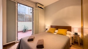 Quarto de hotel com uma cama, duas luminárias de cabeceira, uma janela com vista para uma varanda e uma pequena mesa com abajur.