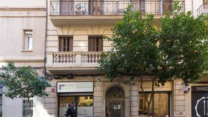 Um edifício com uma placa indicando 'APART EASY', que sinaliza ser um serviço de aluguel de apartamentos. Há uma árvore com laranjas na frente do prédio, uma bicicleta estacionada na calçada e um scooter na rua.