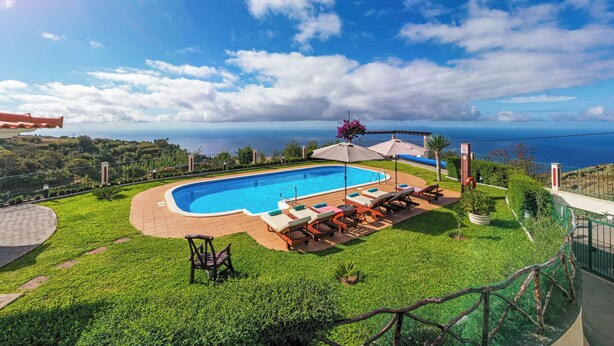 Ein Swimmingpool mit Liegestühlen und Sonnenschirmen, umgeben von einer gepflegten Rasenfläche und einem malerischen Meerblick.