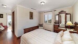 Ein Schlafzimmer mit einem großen Bett, einem Schminktisch, einem Spiegel und einem Fenster mit Blick ins Freie.