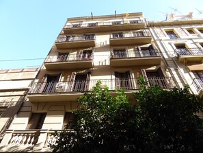 A multi-story building with balconies, a flag, and a tree in the foreground. - Cute, silent and lightly apartment for rent, excellent located in Gracia, Barcelona center (Barcelona)