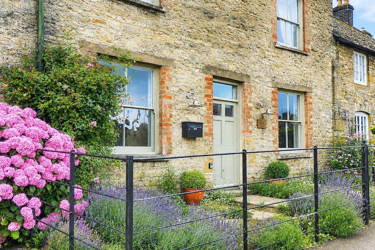 A stone building with multiple windows, a door, and a small garden with flowers.