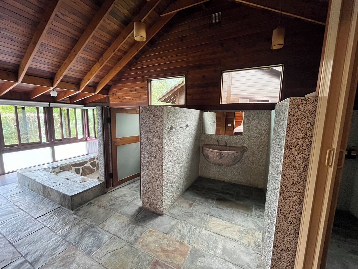 A bathroom with stone flooring, a wooden ceiling, and a window.