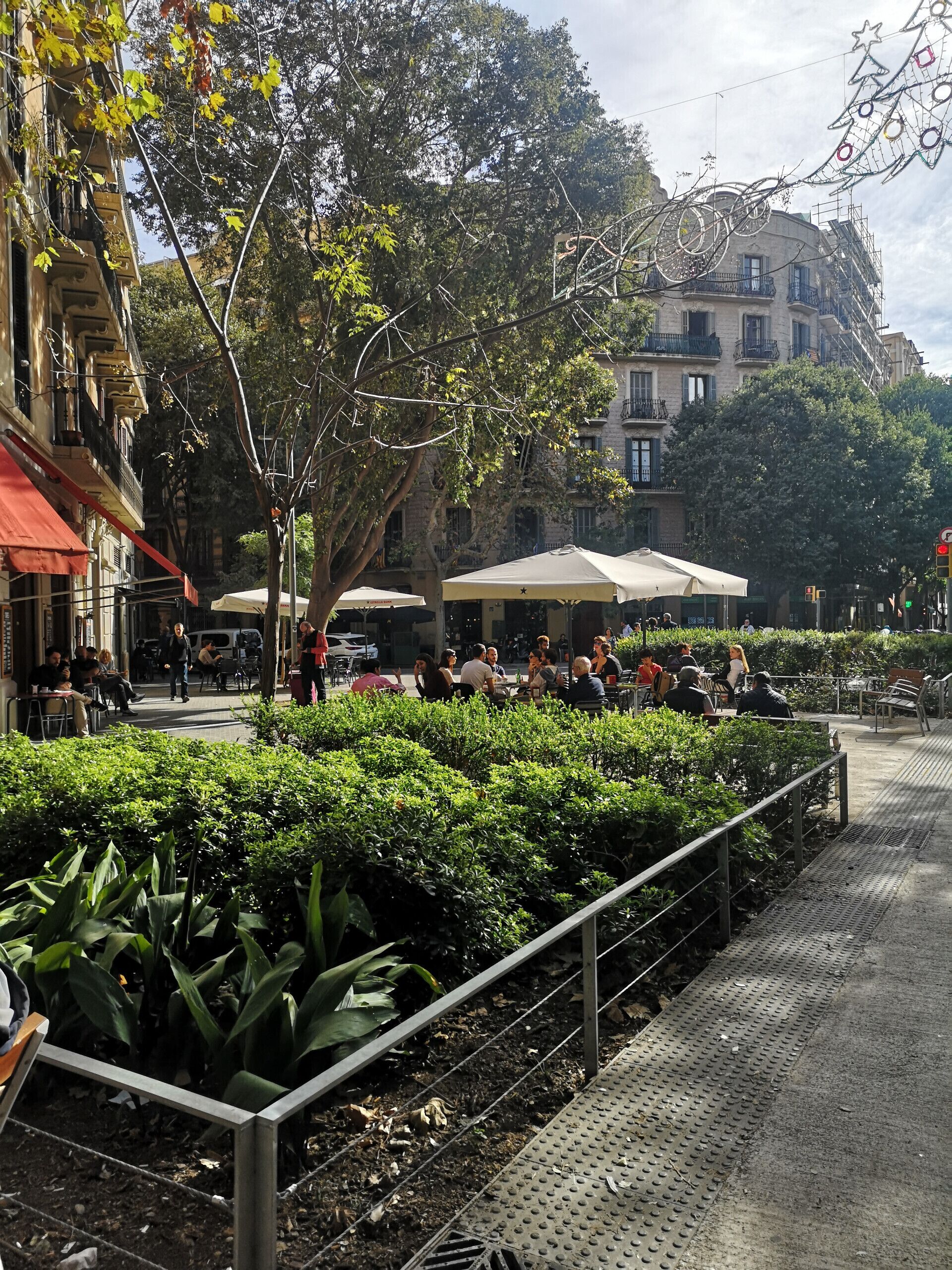 An outdoor café area with tables and chairs, surrounded by greenery and buildings.