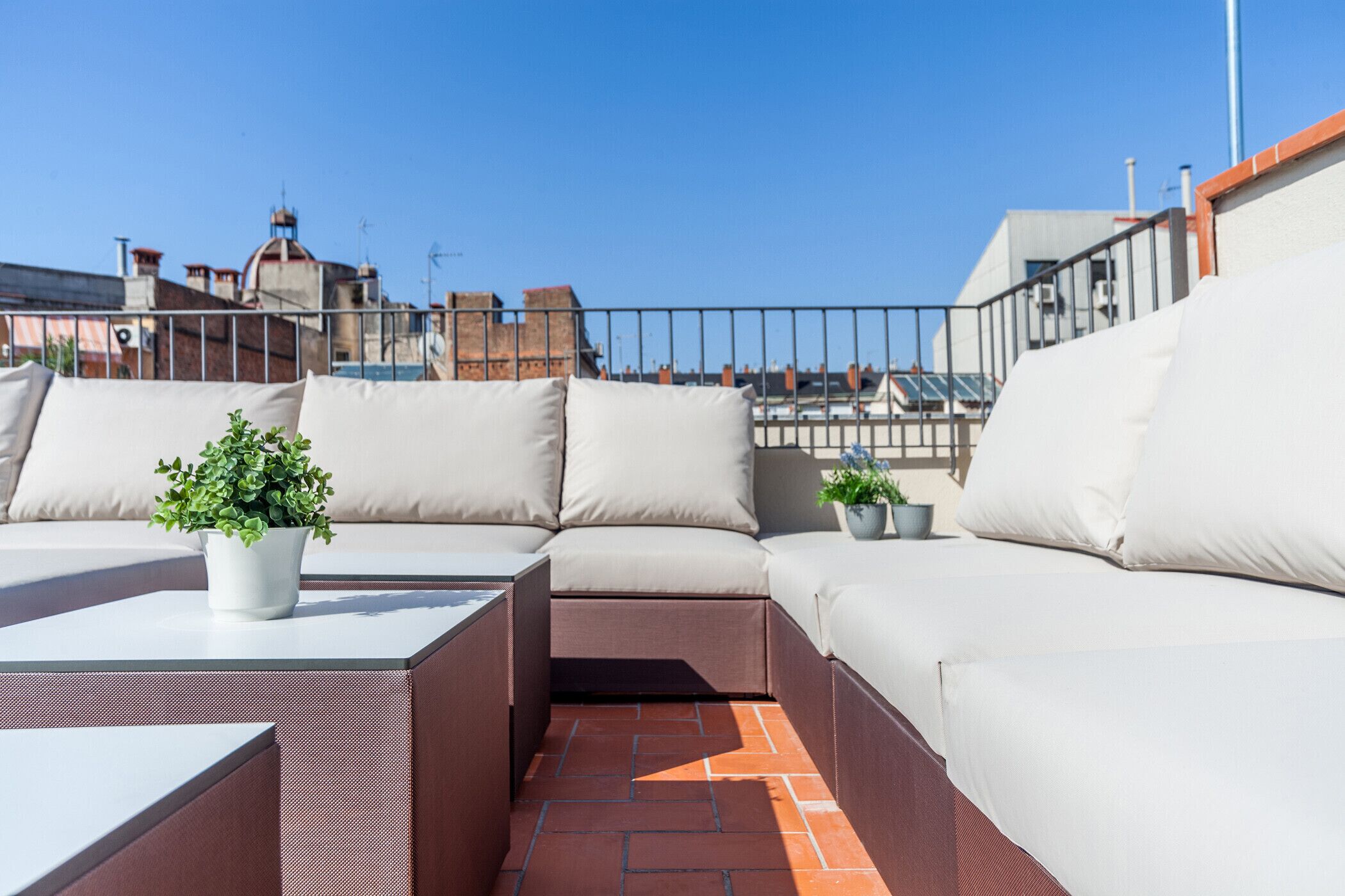 Una terraza en la azotea con un sofá modular, una pequeña mesa y plantas en macetas.