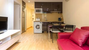 Un espacio habitable compacto con kitchenette, lavadora, zona de comedor con sillas y sofá rojo.
