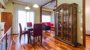Un coin repas avec une table et des chaises en bois, un meuble avec des portes en verre et, au fond, un canapé rouge.